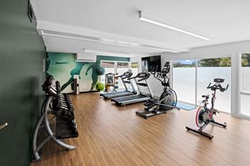 A gym with a row of treadmills and exercise bikes.